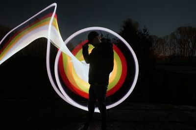 Silhouette man standing by illuminated light against sky at night