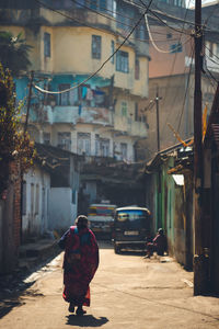 Rear view of woman walking on street amidst buildings in city