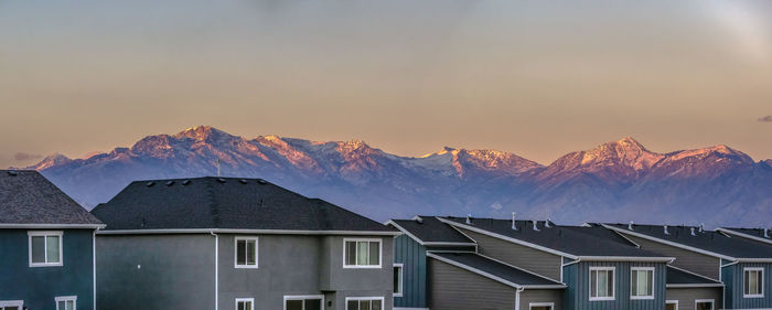 Snow covered houses and mountains against sky during sunset