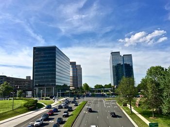 Cars on road by buildings against sky in city