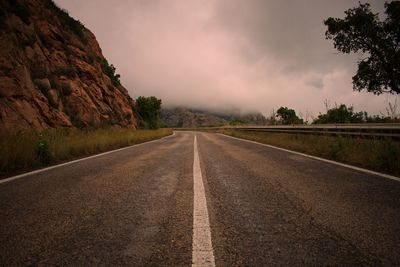 Empty road along trees and against sky