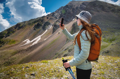 Side view of female blogger taking selfie on smartphone while hiking, discovering wild lands on