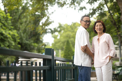 Friends standing on railing against trees