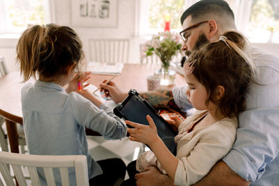 Girl using digital tablet while father assisting daughter in homework at dining table