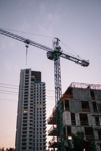 Low angle view of crane by buildings against sky