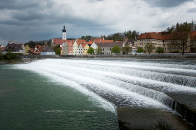 View of town by river against cloudy sky