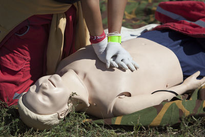 Low section of man practicing cpr on dummy at field during sunny day