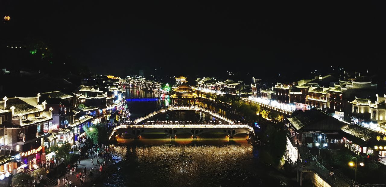 HIGH ANGLE VIEW OF ILLUMINATED BRIDGE OVER RIVER BY BUILDINGS