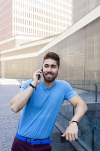 Young businessman talking on phone while standing against building in city