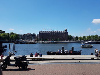 People on pier by river in city against sky