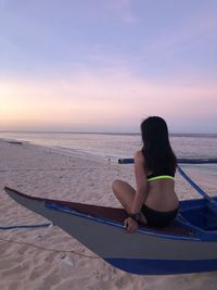 Rear view of woman sitting on beach against sky during sunset