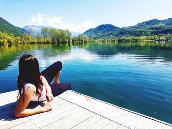 Rear view of woman sitting by lake against sky