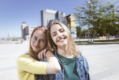 Smiling woman with hands on friend's shoulder in city