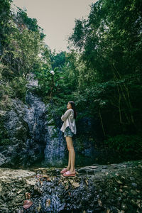 Full length of young woman standing on rock in forest