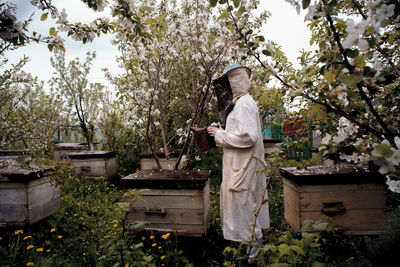 Woman wearing protective workwear while holding beehive smoker at yard