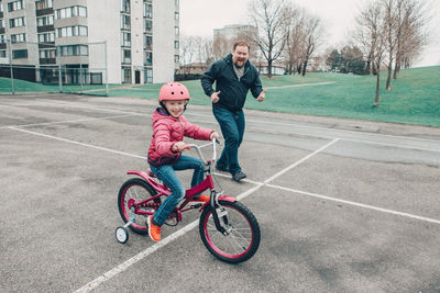 Full length of man encouraging daughter in riding bicycle on walkway