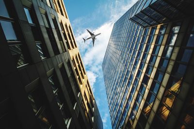 Low angle view of airplane flying over modern buildings against sky