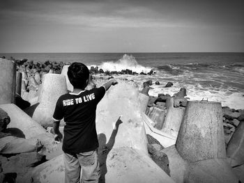 Rear view of boy pointing at sea against sky