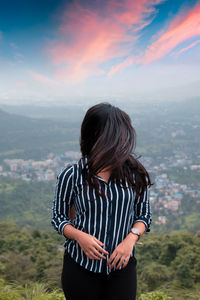 Woman with tousled hair standing on mountain against sky