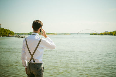 Rear view of man talking on smart phone while standing at beach