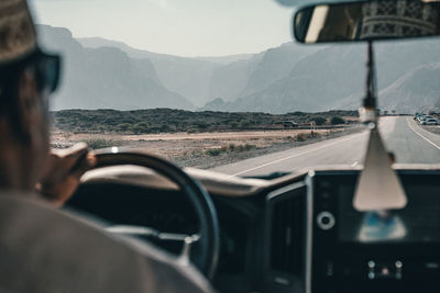 Cropped image of man driving car on highway against mountains