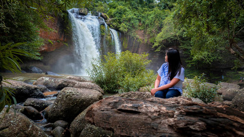 Woman sitting on rock looking at waterfall