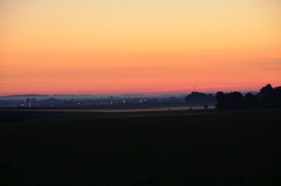 Scenic view of silhouette field against orange sky