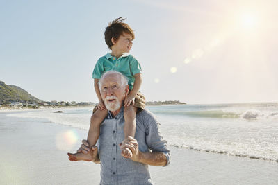 Portrait of senior man with grandson on his shoulders on the beach