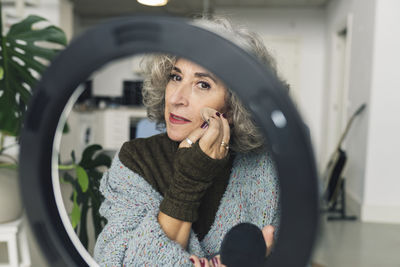 Senior woman applying foundation in front of ring light