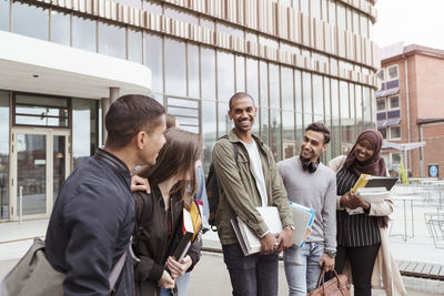 Smiling friends talking while standing at university campus