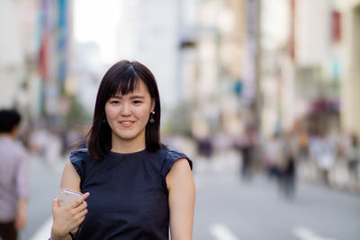 Portrait of smiling young woman standing on street in city