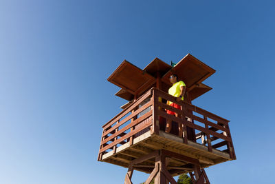 From below male lifeguard controlling safety on sea from wooden rescue tower