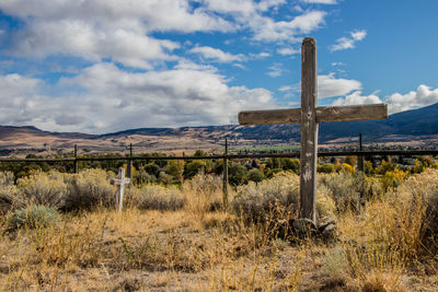 Cross and fence on field against sky