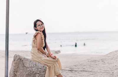 Portrait of woman sitting at beach against sky