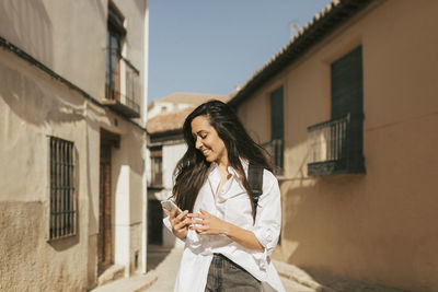 Young woman using phone while standing on building