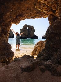 Woman standing on rock by sea against sky