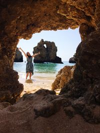 Woman standing at beach seen through cave against sky