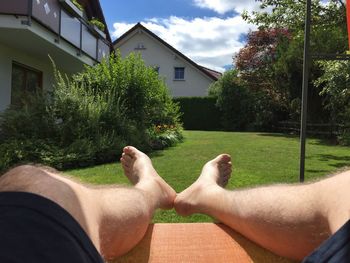 Low section of man relaxing by house against sky