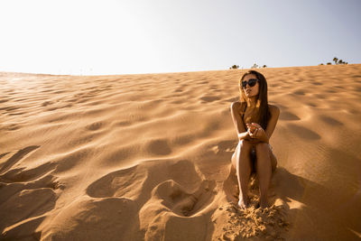 Woman sitting on sand against clear sky