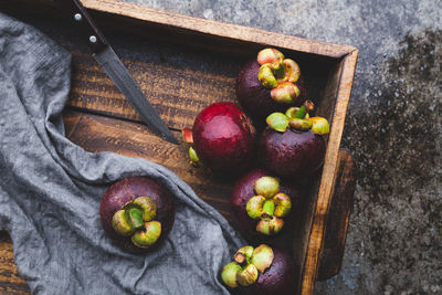 High angle view of purple mangosteens and knife in wooden box