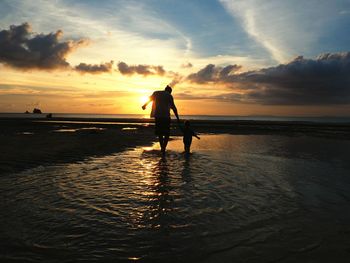 Silhouette men on beach against sky during sunset