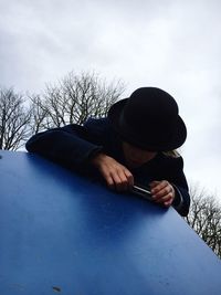 Low angle view of boy wearing hat photographing blue table against sky