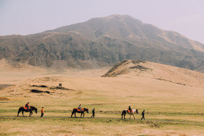 People riding horses in desert against clear sky