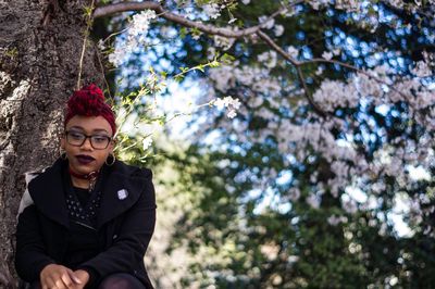 Low angle portrait of punk woman sitting against cherry blossom tree