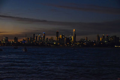 Illuminated city by sea against sky at dusk