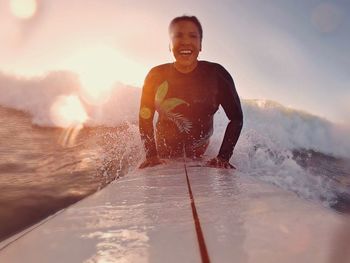 Portrait of smiling woman surfing on sea during sunset