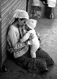 Rear view of mother holding baby girl sitting outdoors
