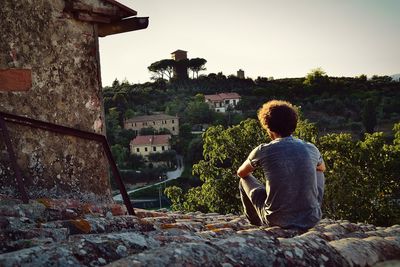Rear view of man sitting on rock against building