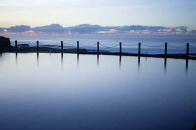 Wooden posts in sea against sky during sunset