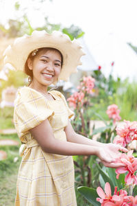Young woman wearing hat standing by flowering plants